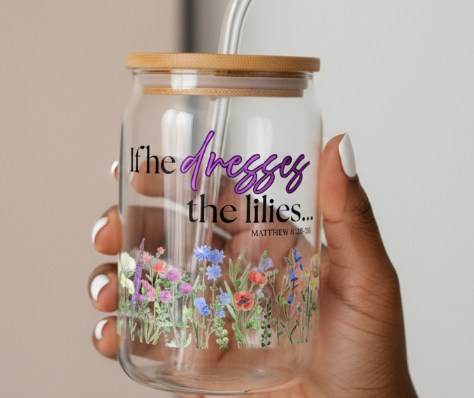 Glass tumbler with floral design and text held by a hand against a neutral background