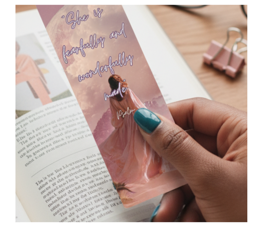 Hand holding a decorative bookmark with a woman in a dress and text on a book page.