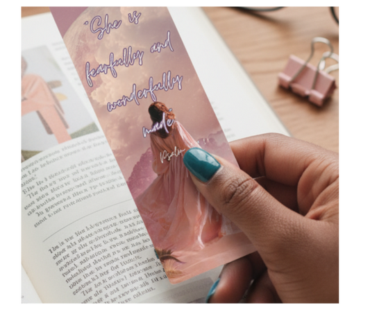 Hand holding a decorative bookmark with a woman in a dress and text on a book page.