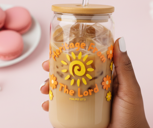 Hand holding a glass mug with a sun design and text, with macarons in the background.