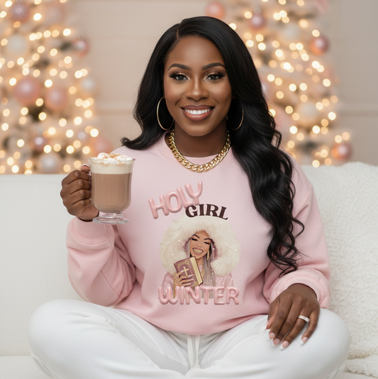 Woman wearing a pink sweatshirt with a graphic design, sitting on a couch holding a hot beverage with Christmas decorations in the background.