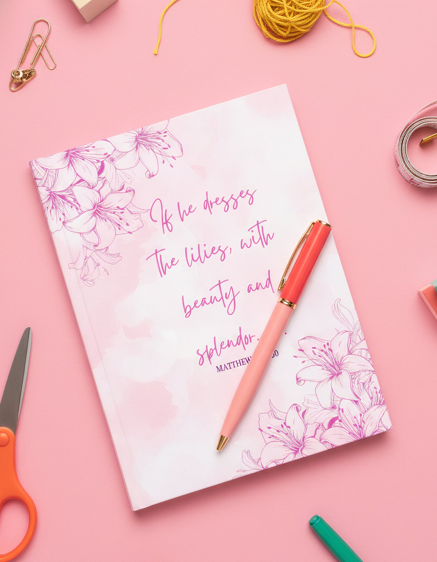 Notebook with floral design and text on a pink background with stationery items.
