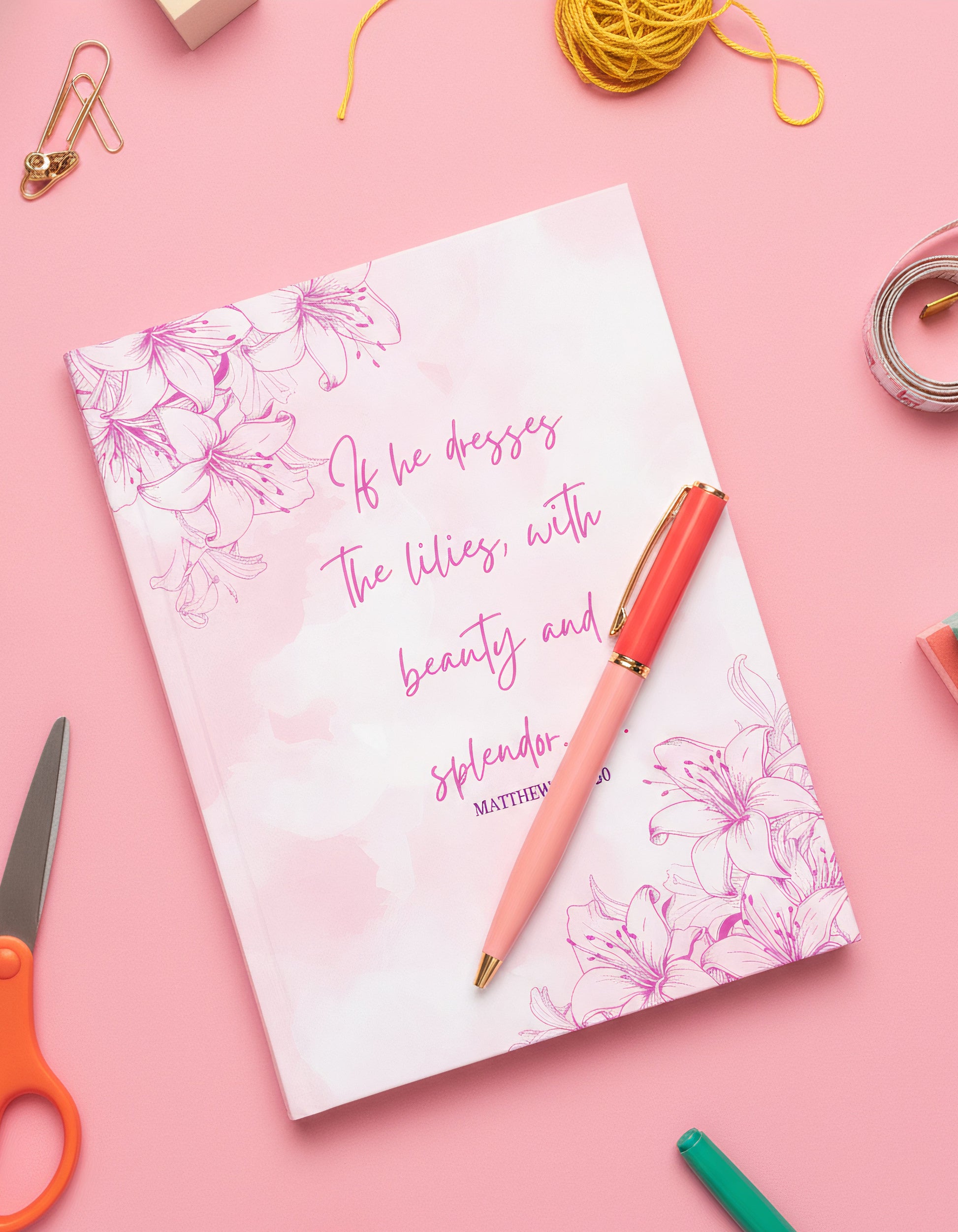 Notebook with floral design and text on a pink background with stationery items.