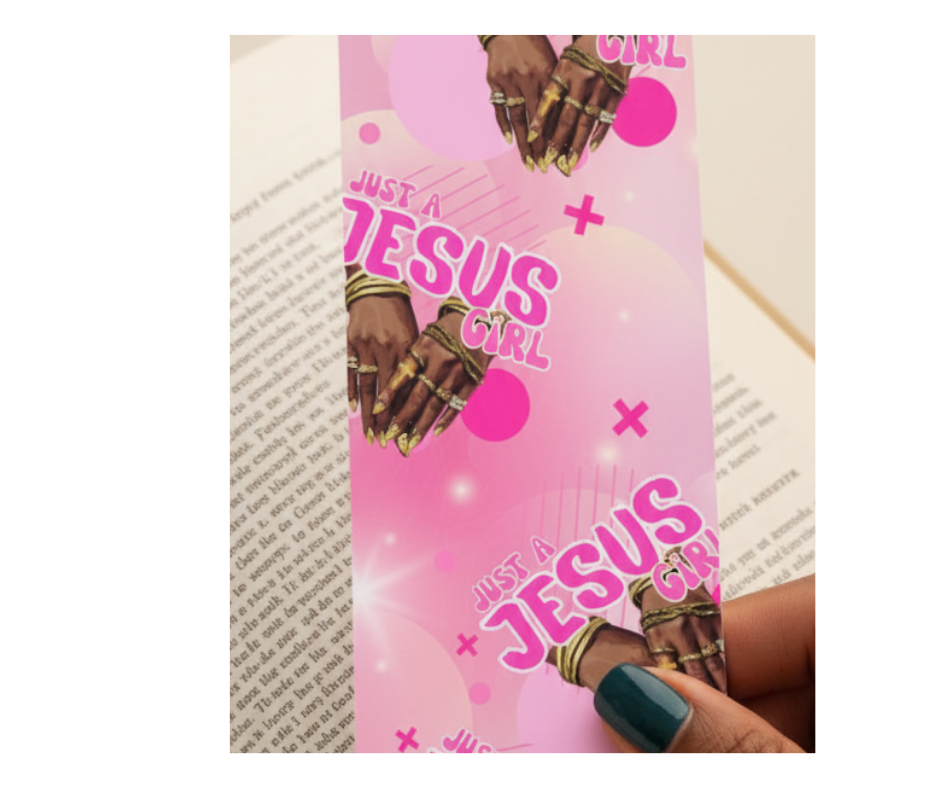 Pink bookmark with 'Just a Jesus Girl' text and hands holding it, on a book page background.