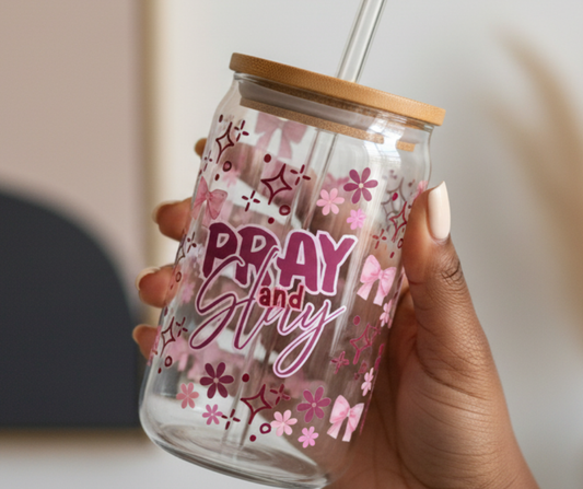 Hand holding a glass tumbler with floral designs and 'Pray and Slay' text.