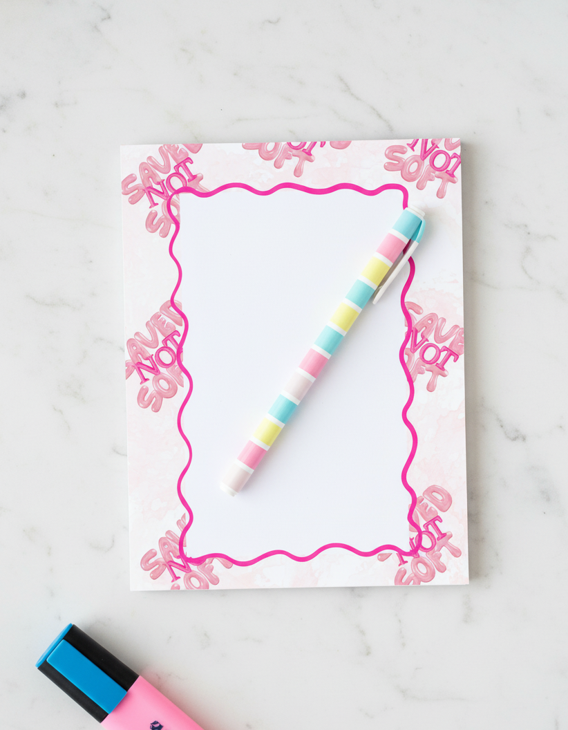 Notebook with pink floral border and colorful pen on a white marble surface