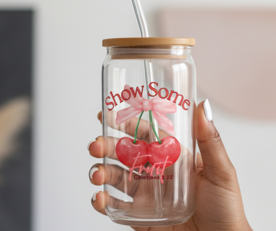 Clear tumbler with cherry design and text held by a hand against a neutral background