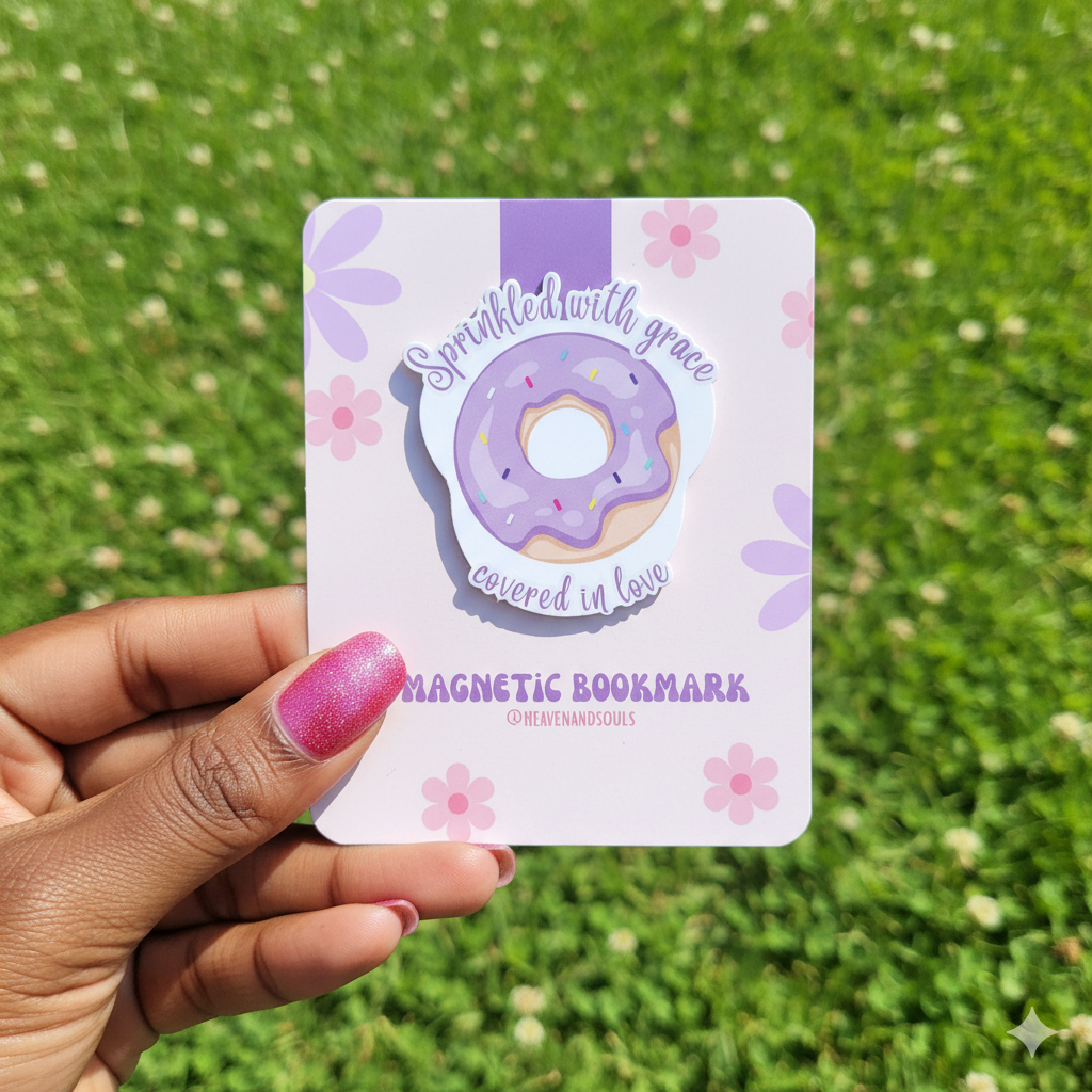 Hand holding a magnetic bookmark with a donut design against a grassy background